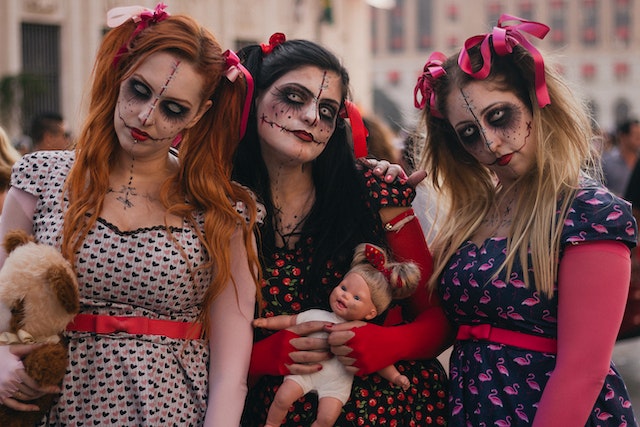 Three girls dressed as dolls and carrying dolls in their hands