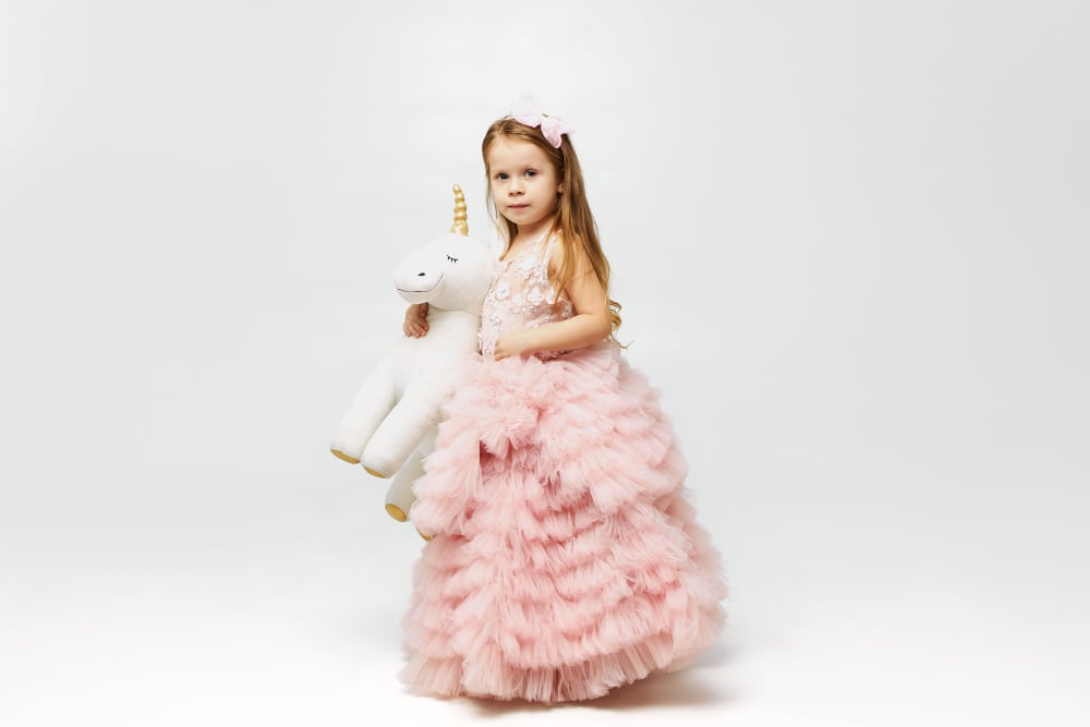 a litttle girl wearing pink princess dress and holding a unicorn doll