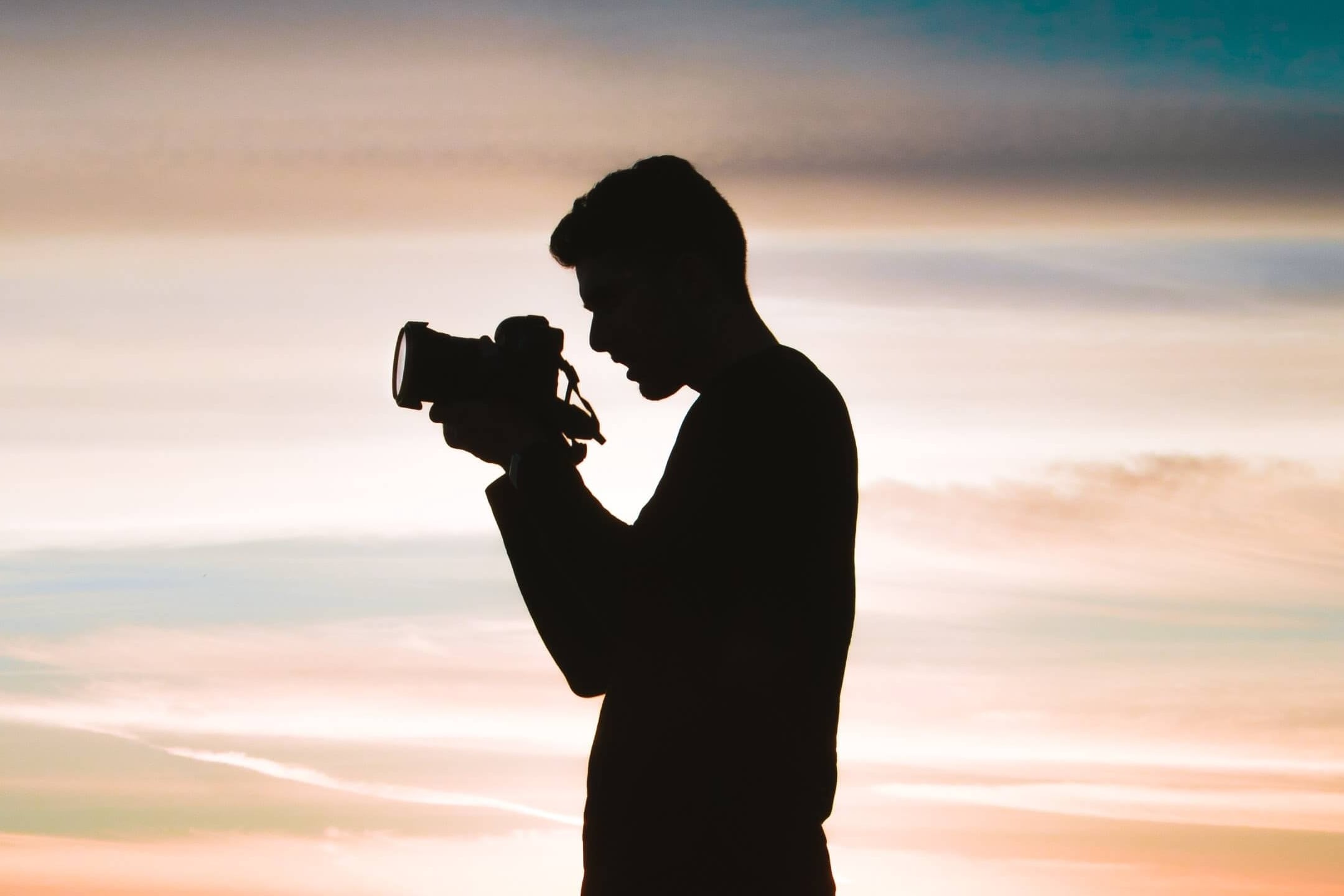 a shadow of a boy carrying the camera with red sky behind